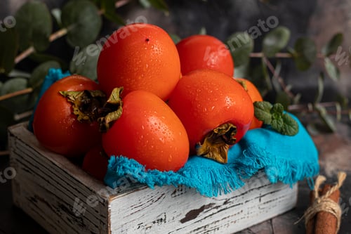 Preview: Persimmon on a dark background. Fresh, ripe fruits on a blue plate and in a box. Healthy eating.