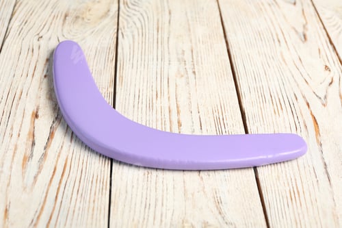 Preview: Purple boomerang on white wooden background. Outdoors activity