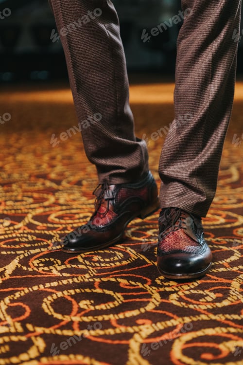 Preview: Vertical shot of a stylish man in textured brown suit pants and brown and black brogue shoes