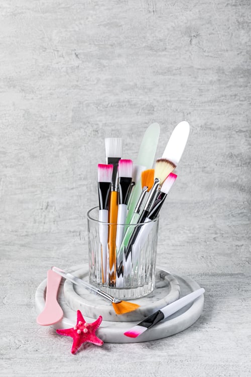 Preview: A variety of brushes and spatulas for applying face mask on grey background.
