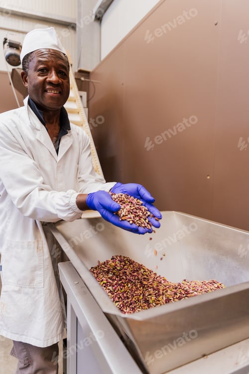 Preview: Worker smiling while holding dry pistachios in warehouse