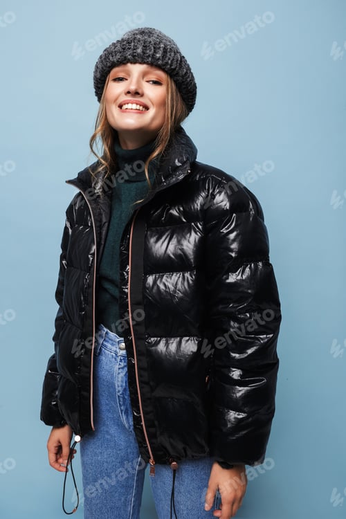Preview: Young pretty smiling woman in knitted hat and black down jacket joyfully looking in camera