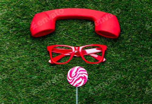 Preview: styled red glasses with lollipop and handset on green grass background,