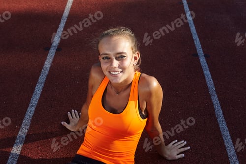 Preview: Portrait of young female runner sitting on race track