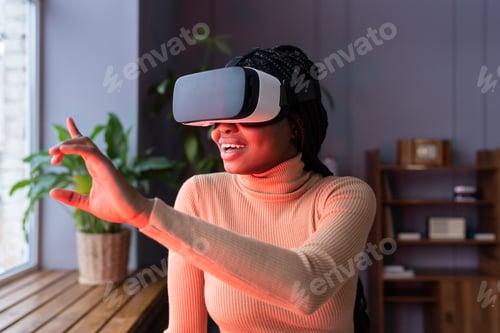 Preview: Excited african american woman testing VR helmet while sitting in red neon light in cozy office
