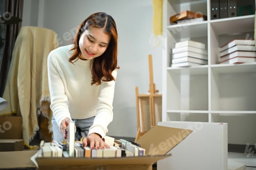 Preview: Smiling asian woman moving into new home, unpacking parcel box on floor in living room