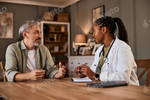 Preview: An African female doctor talking with a senior male patient during a home visit.