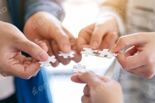 Preview: Closeup image of many people holding and putting a piece of white jigsaw puzzle together