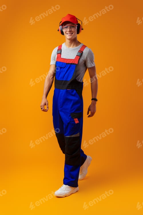 Preview: Young construction worker in uniform posing on yellow background in studio