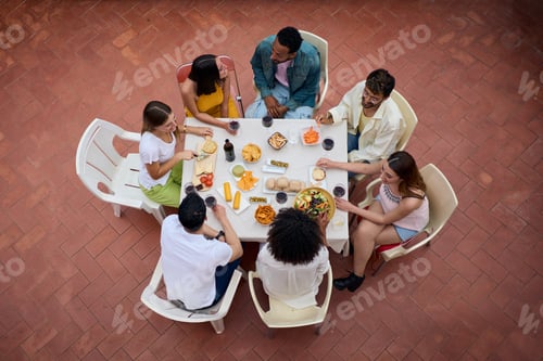 Preview: Top view from above of a gathering of people around a table with glasses of wine and food