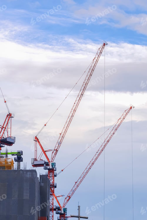 Preview: Group of tower cranes working on top of high building structure against cloudy sky background