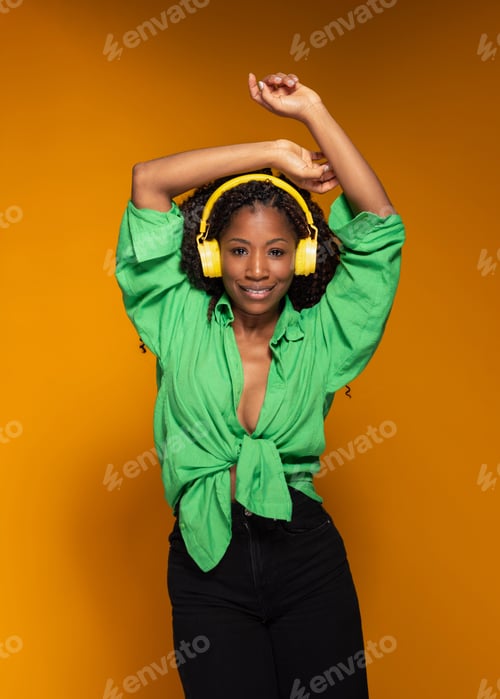 Preview: Smiling Hispanic woman with headphones listening to music and dancing on yellow background