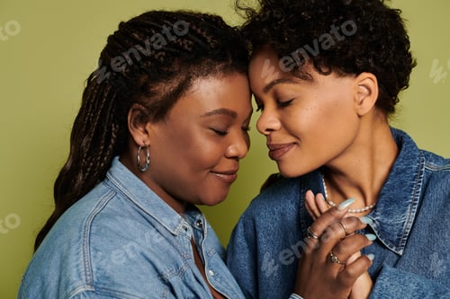 Preview: Stylish lesbian couple sharing a loving moment against a vibrant green backdrop