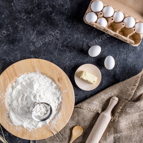 Preview: top view of raw eggs, flour, butter and kitchenware for bakery on dark tabletop
