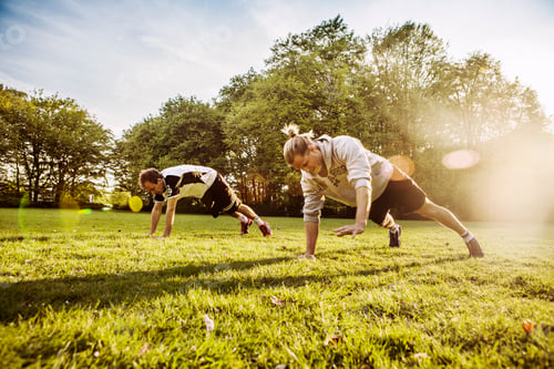 Vista previa: Young men doing push-ups on grassy field on sunny day