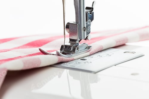 Preview: Close-up of sewing machine needle stitching red and white striped fabric in a bright workspace