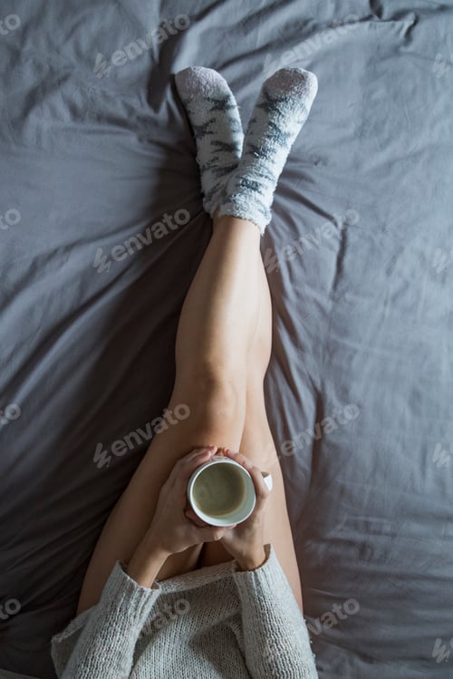 Preview: top view of unrecognizable woman legs enjoying coffee on bed in bedroom. home and lifestyle
