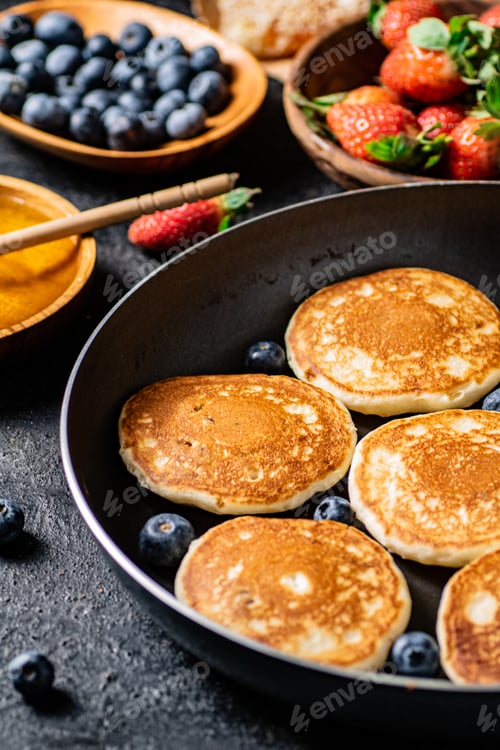 Vista previa: Pancakes in a frying pan with fresh berries and honey.