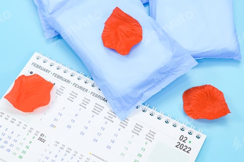 Preview: Three female pads, desk calendar for February 2022 and artificial rose petals on a light blue .