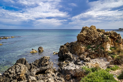 Preview: Landscape of the sea surrounded by rocks under a cloudy sky and sunlight