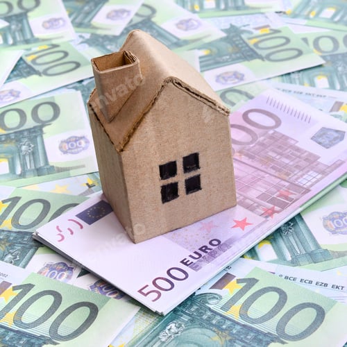 Preview: Small toy house is lies on a set of green monetary denominations of 100 euros