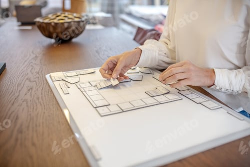 Preview: Female hands collecting interior layout of a room on a table.