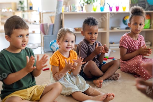 Preview: Group of small nursery school children sitting on floor indoors in classroom, clapping