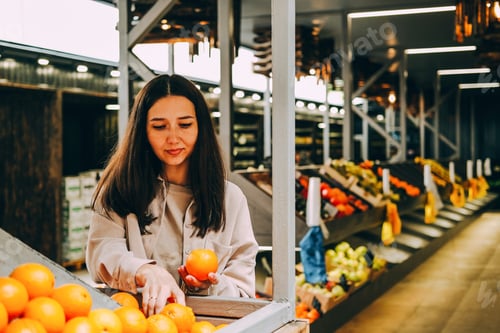 Preview: Young beautiful dark-haired woman holds oranges in market