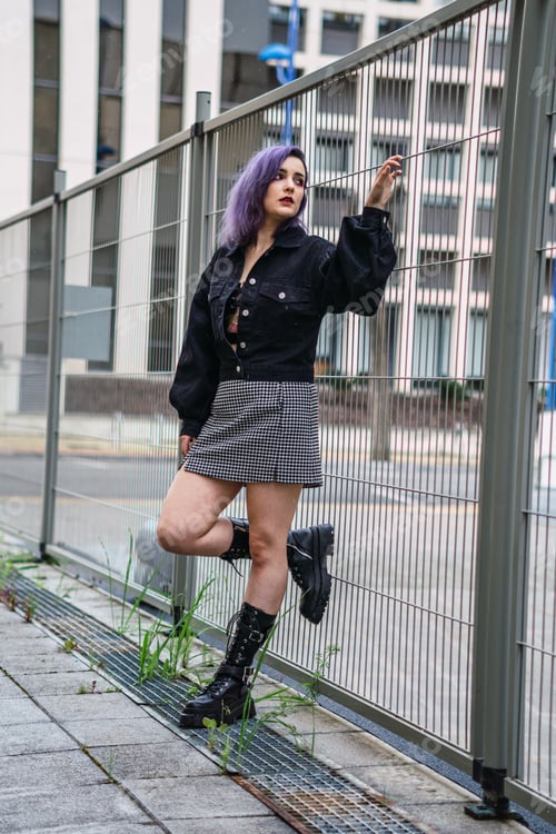 Preview: Vertical shot of a sexy Caucasian woman with purple hair and red lipstick leaning on the fence