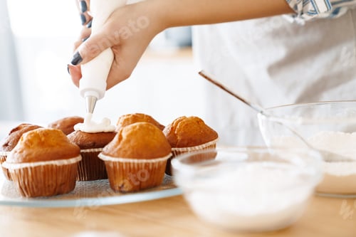 Preview: Cropped image of young caucasian woman cooking muffins with cream