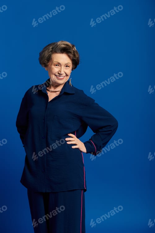 Preview: A stylish woman in her 60s poses confidently against a bright blue backdrop.