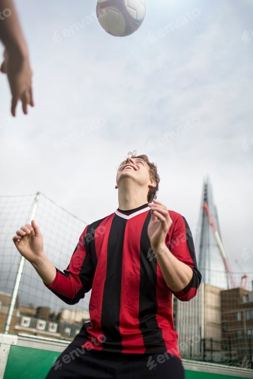 Preview: Young man practising football skills on urban football pitch