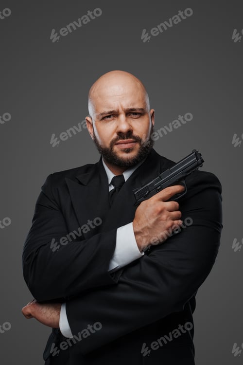 Preview: Bald and bearded man in a black suit holds a pistol, exuding power