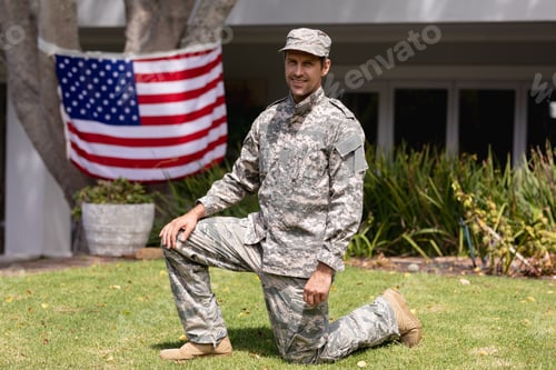 Preview: Smiling caucasian soldier father kneeling in garden with american flag hanging outside house