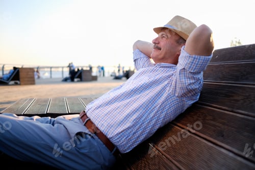 Preview: Senior hispanic man in summer hat sitting outdoors on bench.