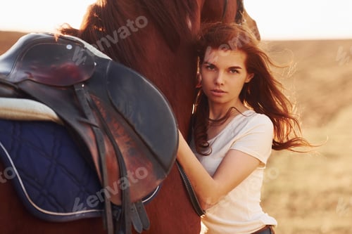 Preview: Young woman embracing her horse in agriculture field at sunny daytime