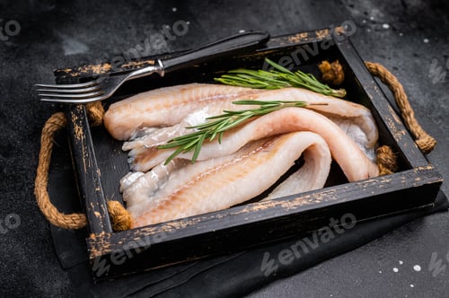 Preview: Ready for cooking Raw Hake fish fillets in a wooden tray with herbs. black background. top view