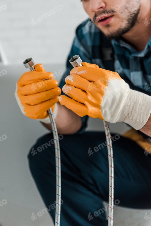 Preview: selective focus of bearded repairman holding metal hose