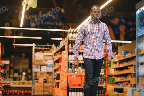 Preview: Portrait of smiling man at supermarket. Young african man with shopping basket in grocery store