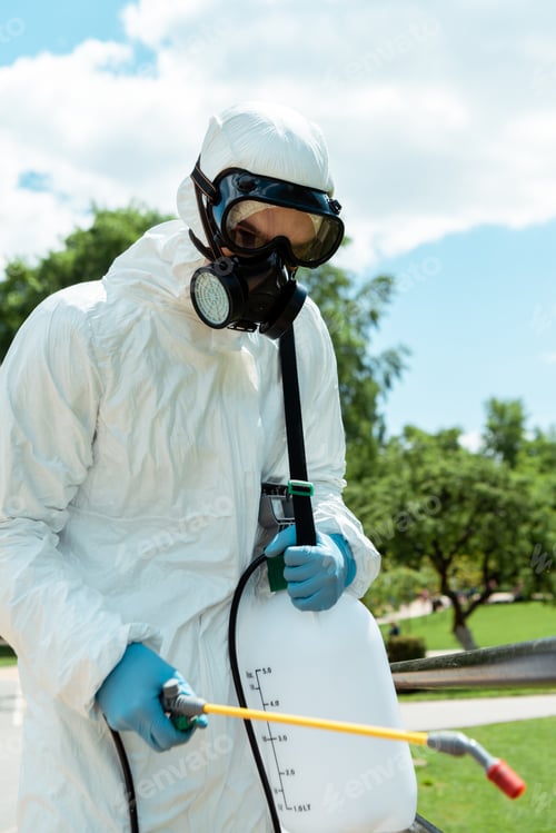 Preview: specialist in hazmat suit and respirator disinfecting park during coronavirus pandemic
