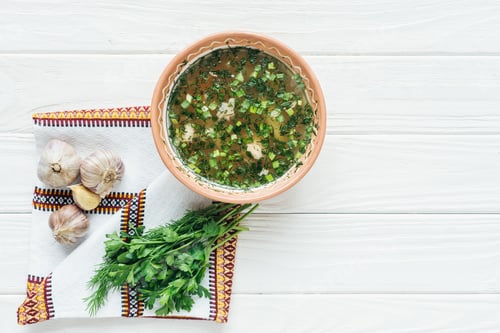Preview: top view of traditional fish soup with green onion, embroidered towel and greens on white wooden