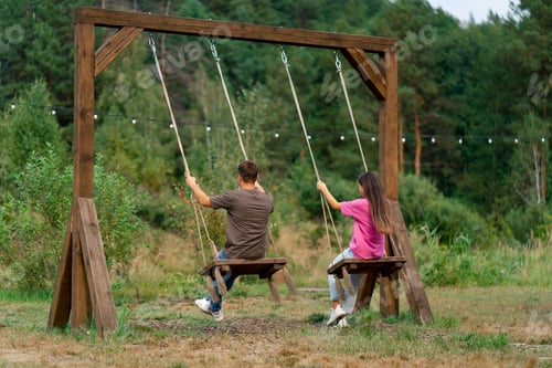 Preview: Loving couple man and girl riding on a large wooden swing overlooking a beautiful lake in nature