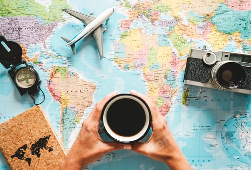 Preview: Top view of young woman planning her vacation using world map while drinking coffee