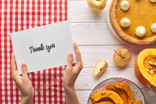 Preview: partial view of woman holding thank you card near pumpkin pie on wooden white table with apples