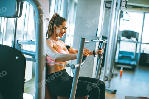 Preview: Young determined fitness woman doing exercises at chest press machine at modern gym