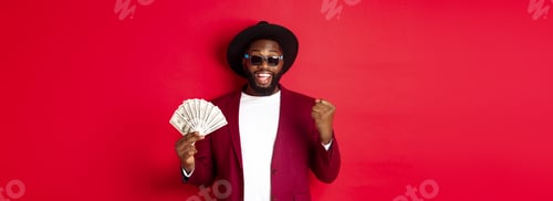 Preview: Cheerful african american guy in sunglasses, black hat and blazer, winning prize money, holding