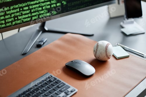Preview: Closeup of Computer Mouse and Baseball on Desk with Programming Code Displayed