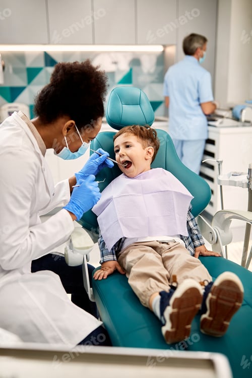 Preview: African American dentist examining teeth of a small boy at dentist's office.