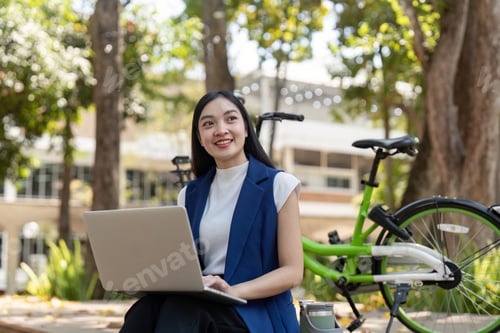 Preview: Friendly businesswoman working on a laptop in a sustainable eco friendly setting with bicycle