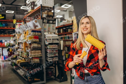 Preview: Young independent woman buying paintbrush and tools for house decoration in hardware store.